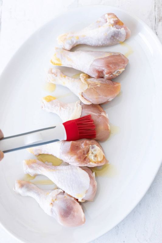 Person basting olive oil on unbaked chicken legs.
