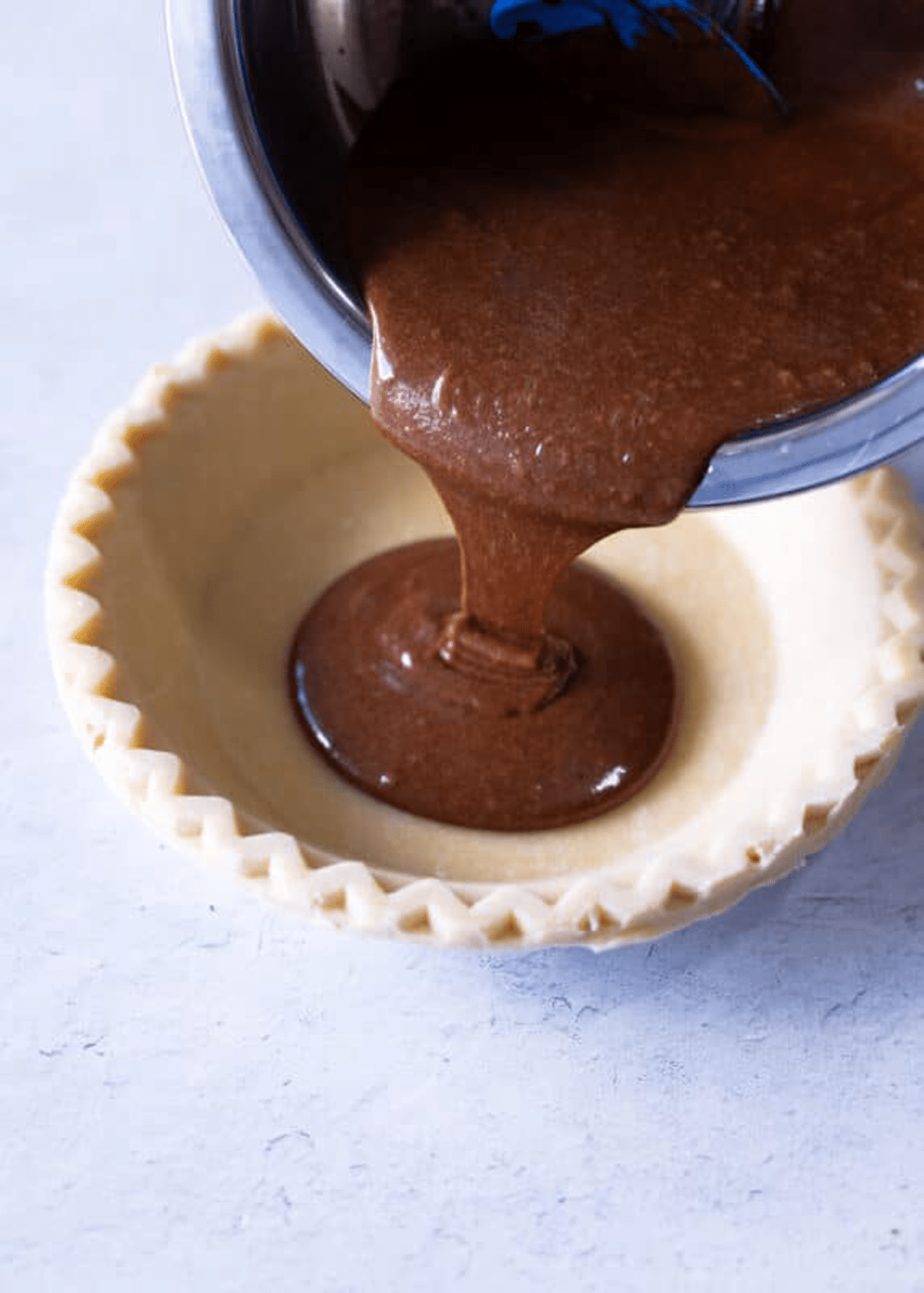 Person pouring chocolate pie filling in a pie shell.