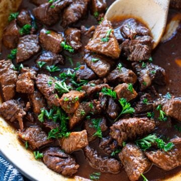 Person stirring garlic steak bites in a large pan.