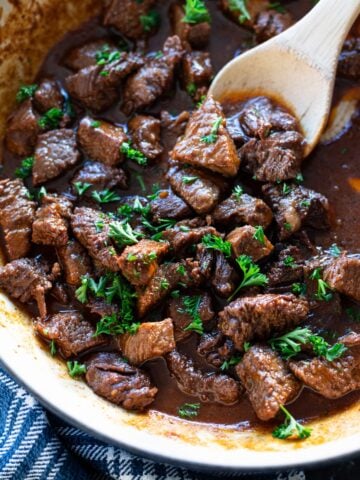 Person stirring garlic steak bites in a large pan.