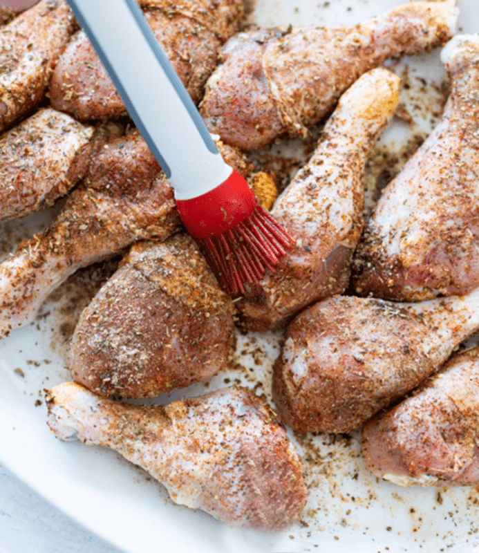 Person basting oil and seasoning onto each piece of chicken leg.