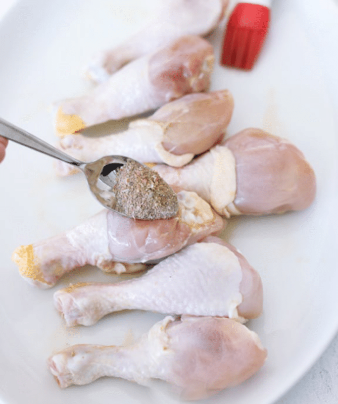Person adding seasoning to chicken drumsticks.