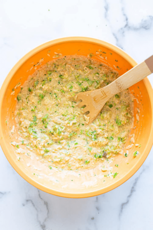 Person using a wooden spoon to stir broccoli and cheese sauce.
