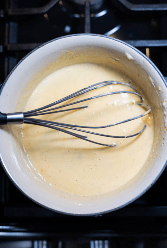 Whisking cheese sauce in a saucepan.