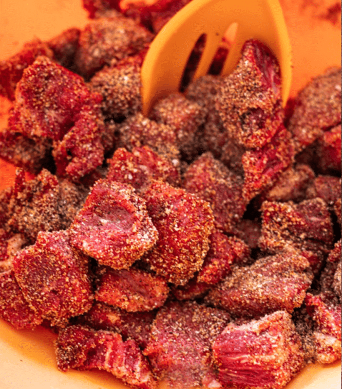 Person stirring steak bites in a bowl with seasoning.