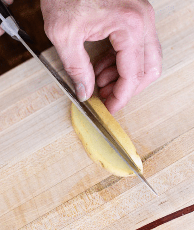 Person cutting a piece of potato in a ½ inch quarter.
