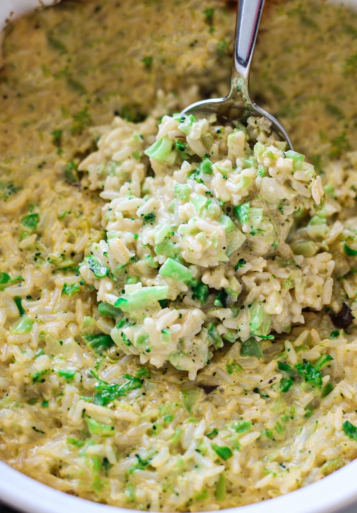 Person spooning a rice and broccoli casserole from a glass dish.