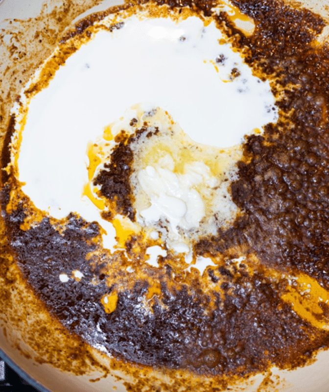 Heavy whipping cream being added to a pan on a stove top.