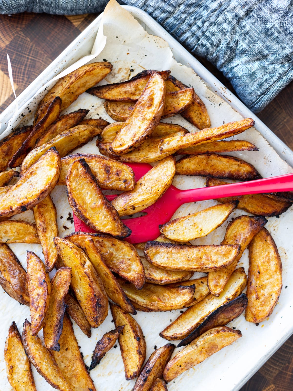 Person flipping over steak fries in a baking dish.